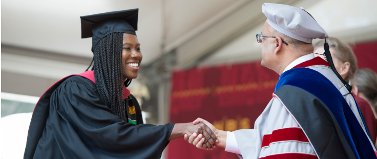 MBA student and dean Nitin Nohria shaking hands on commencement stage